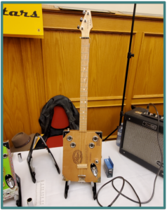 Edmonton Guitar Show- Image of an a cigar box guitar body with resonator holes and full scale with jack and controls